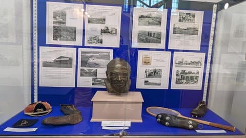 Colour photo of display case from the Schofield exhibition.  Includes printed text and photos, artefacts, and a bust of Herbert Schofield.